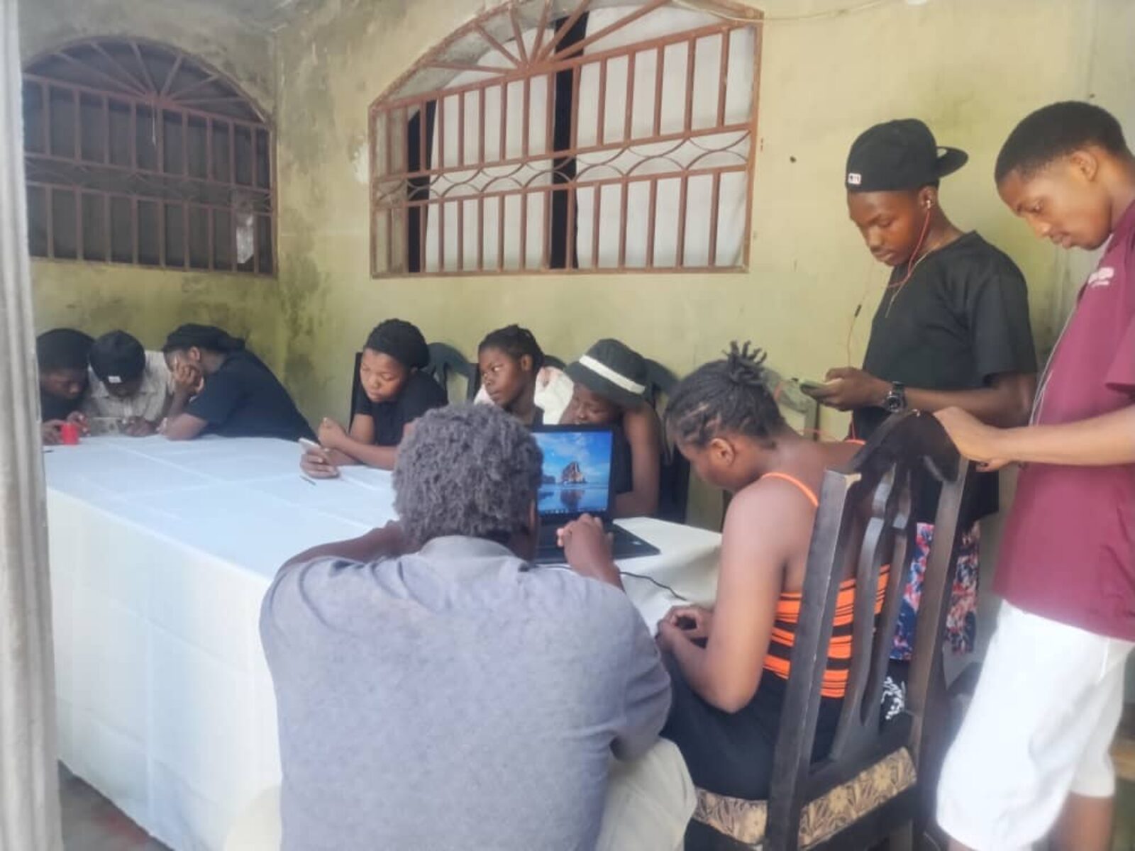 Jèn adilt ann Ayiti reyini otou yon sèl laptop ak telefòn yo pandan yon fòmasyon IA an dirèk.